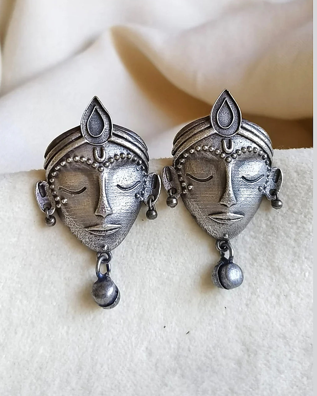 Oxidised silver-look brass stud earrings shaped as crowned goddess faces, each with a small bell drop