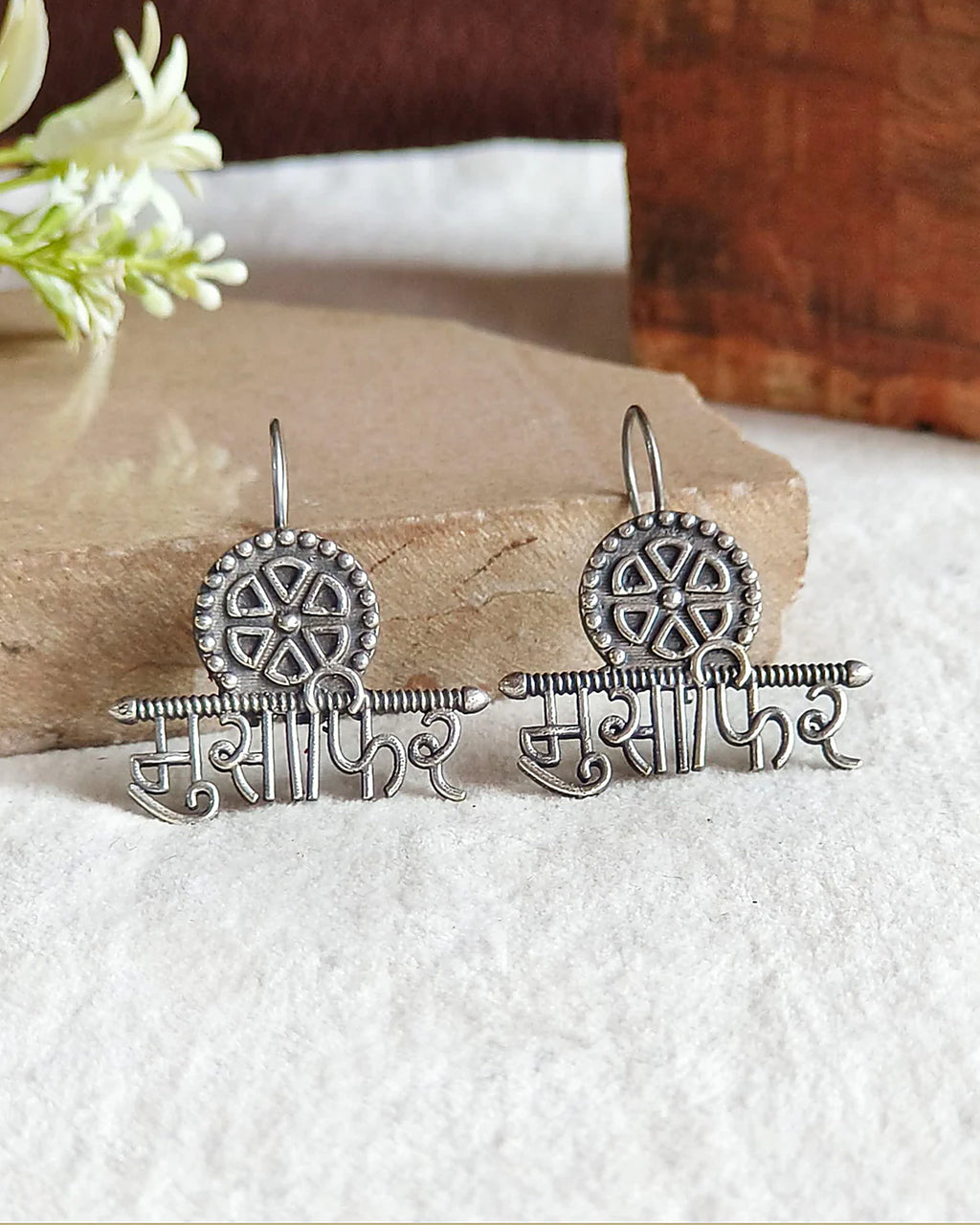 Oxidised silver-look brass drop earrings with the Devanagari word मुसाफ़िर beneath a spoked wheel