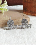 Oxidised silver-look brass drop earrings with the Devanagari word मुसाफ़िर beneath a spoked wheel