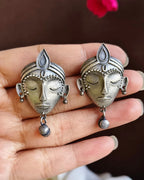Oxidised silver-look brass stud earrings shaped as crowned goddess faces, each with a small bell drop