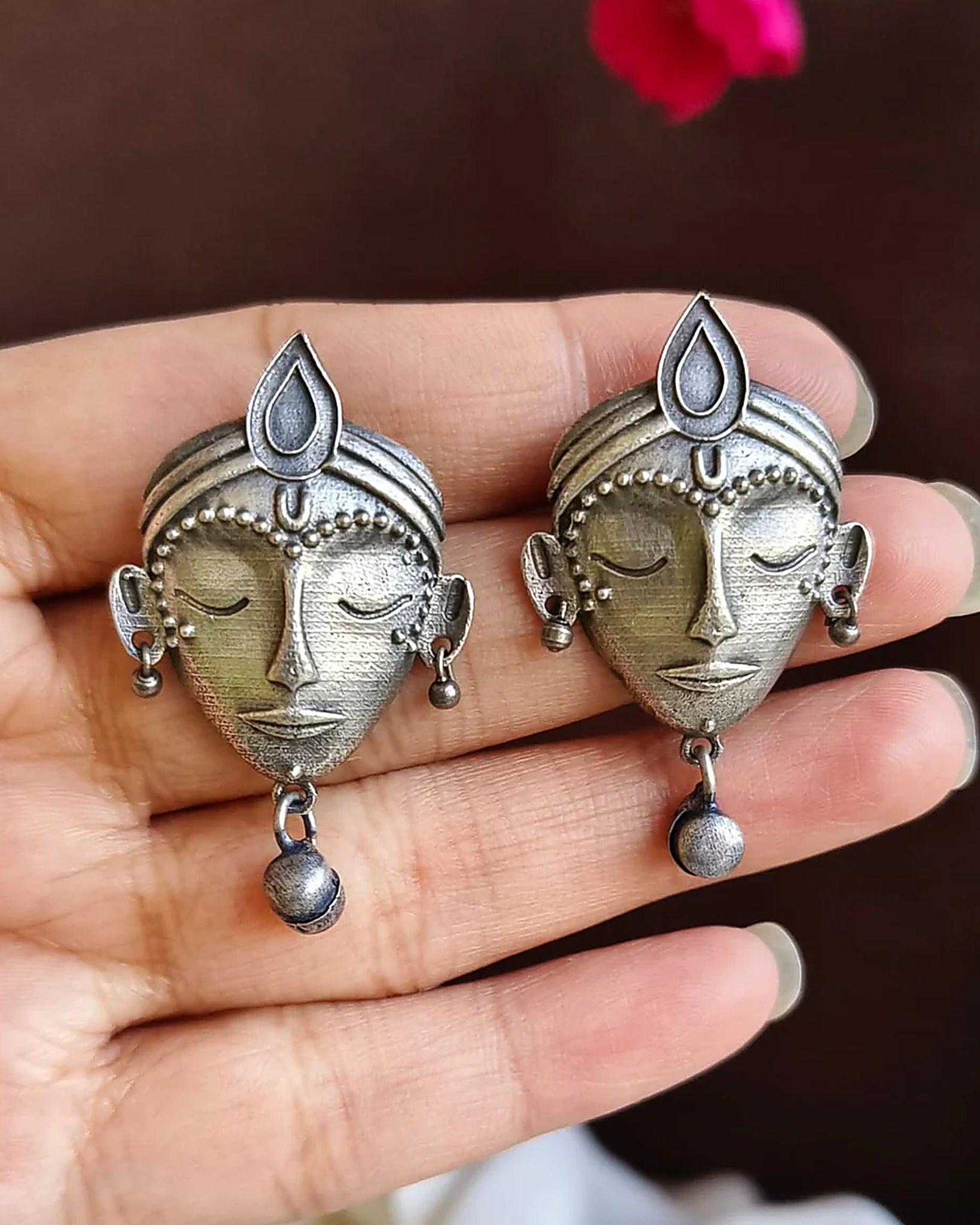 Oxidised silver-look brass stud earrings shaped as crowned goddess faces, each with a small bell drop