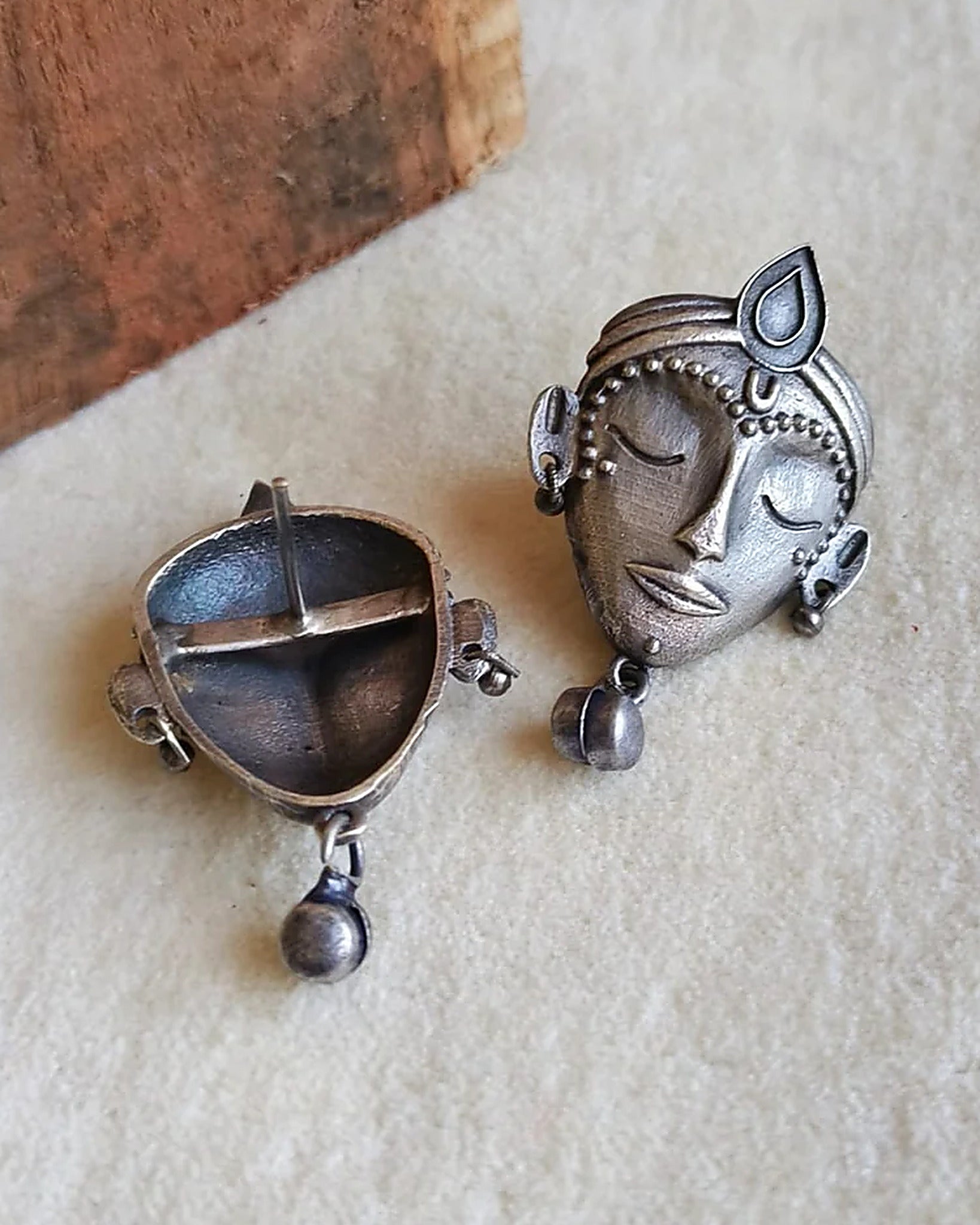 Oxidised silver-look brass stud earrings shaped as crowned goddess faces, each with a small bell drop