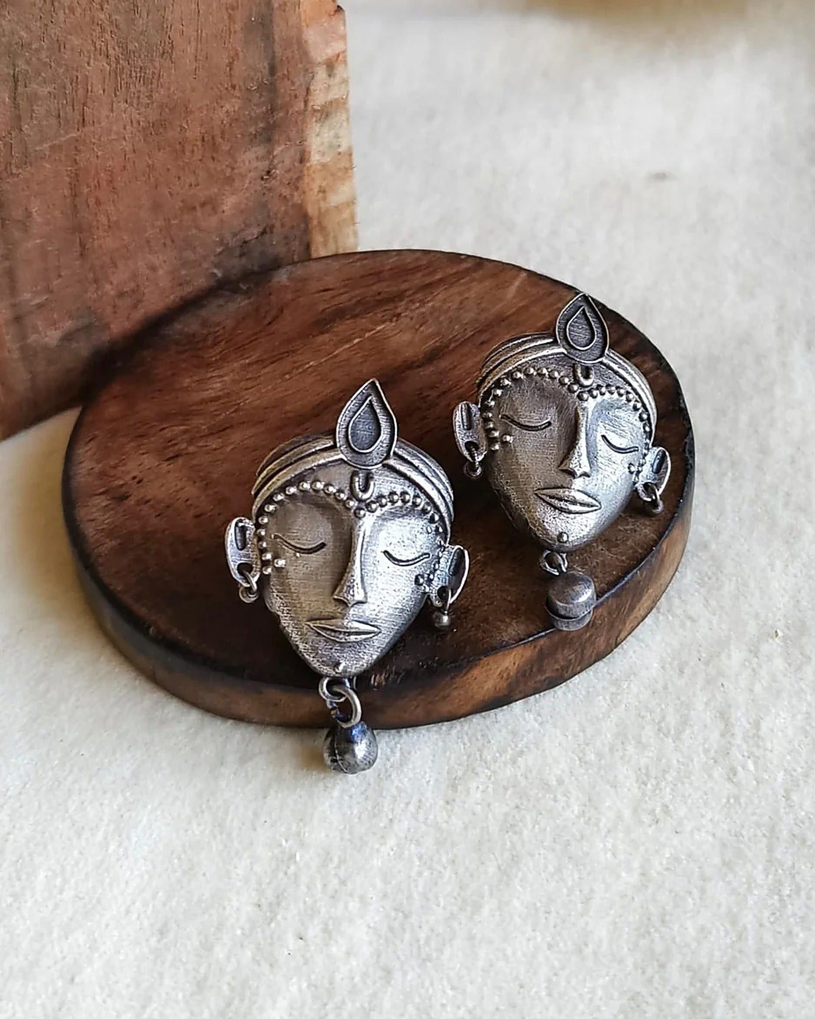 Oxidised silver-look brass stud earrings shaped as crowned goddess faces, each with a small bell drop
