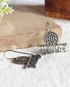 Oxidised silver-look brass drop earrings with the Devanagari word मुसाफ़िर beneath a spoked wheel