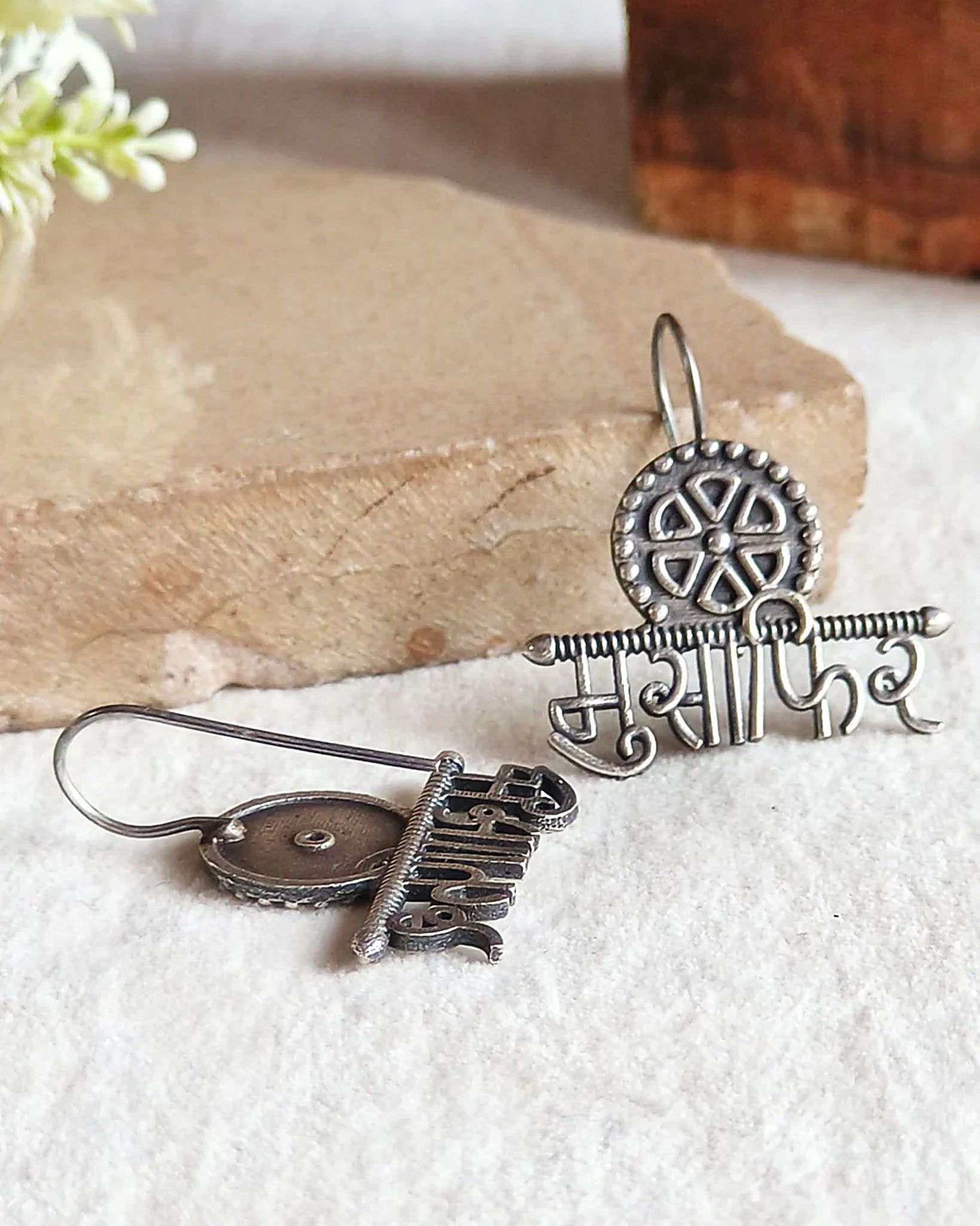 Oxidised silver-look brass drop earrings with the Devanagari word मुसाफ़िर beneath a spoked wheel