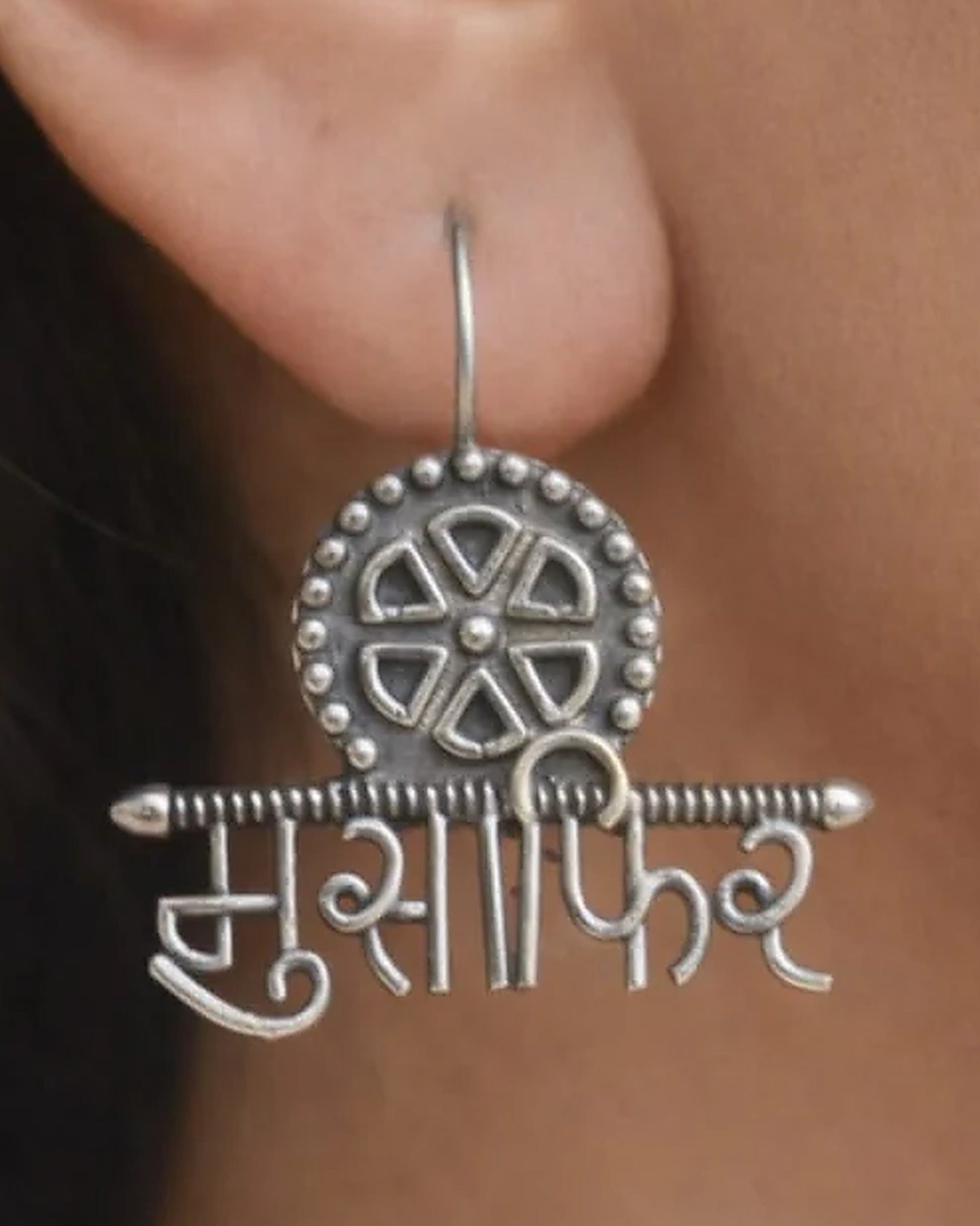 Oxidised silver-look brass drop earrings with the Devanagari word मुसाफ़िर beneath a spoked wheel