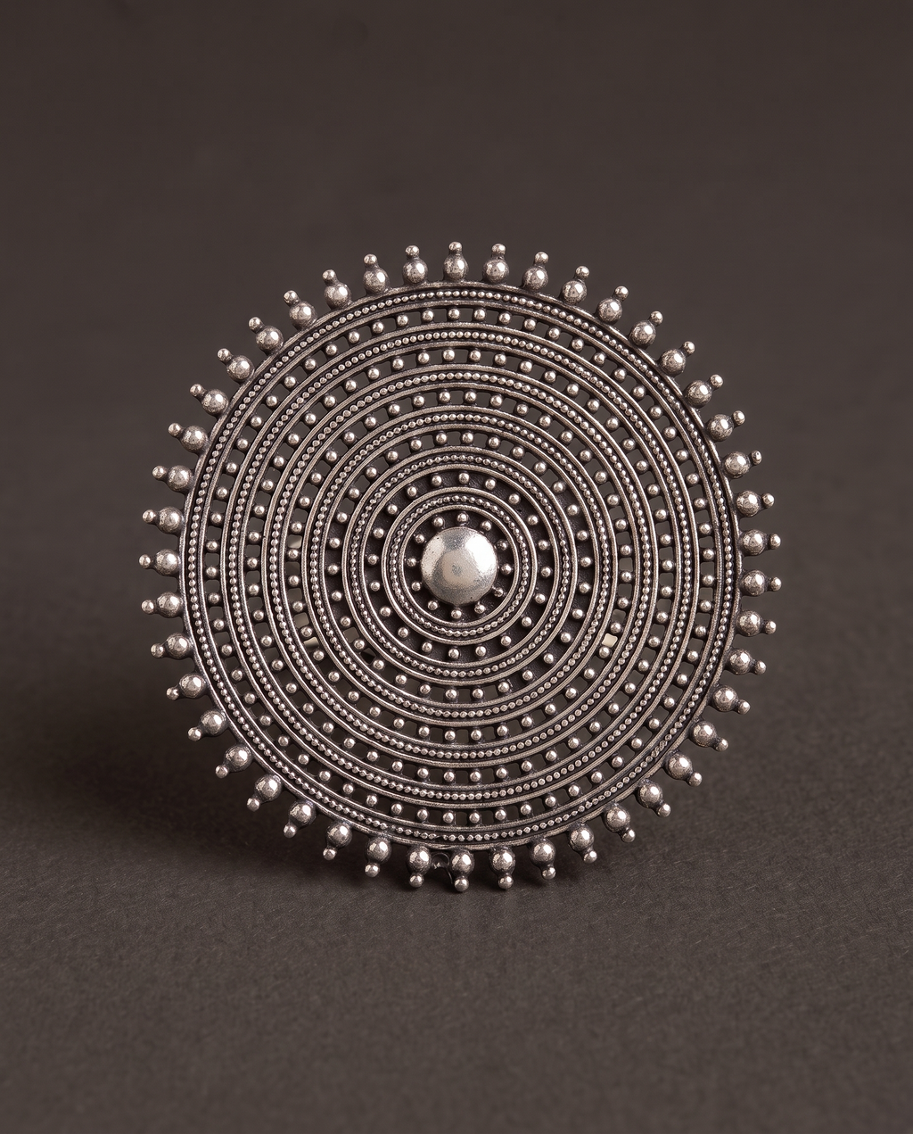 Close-up of the Nishan concentric disc ring on charcoal, showing the fine beaded granulation and smooth domed centre