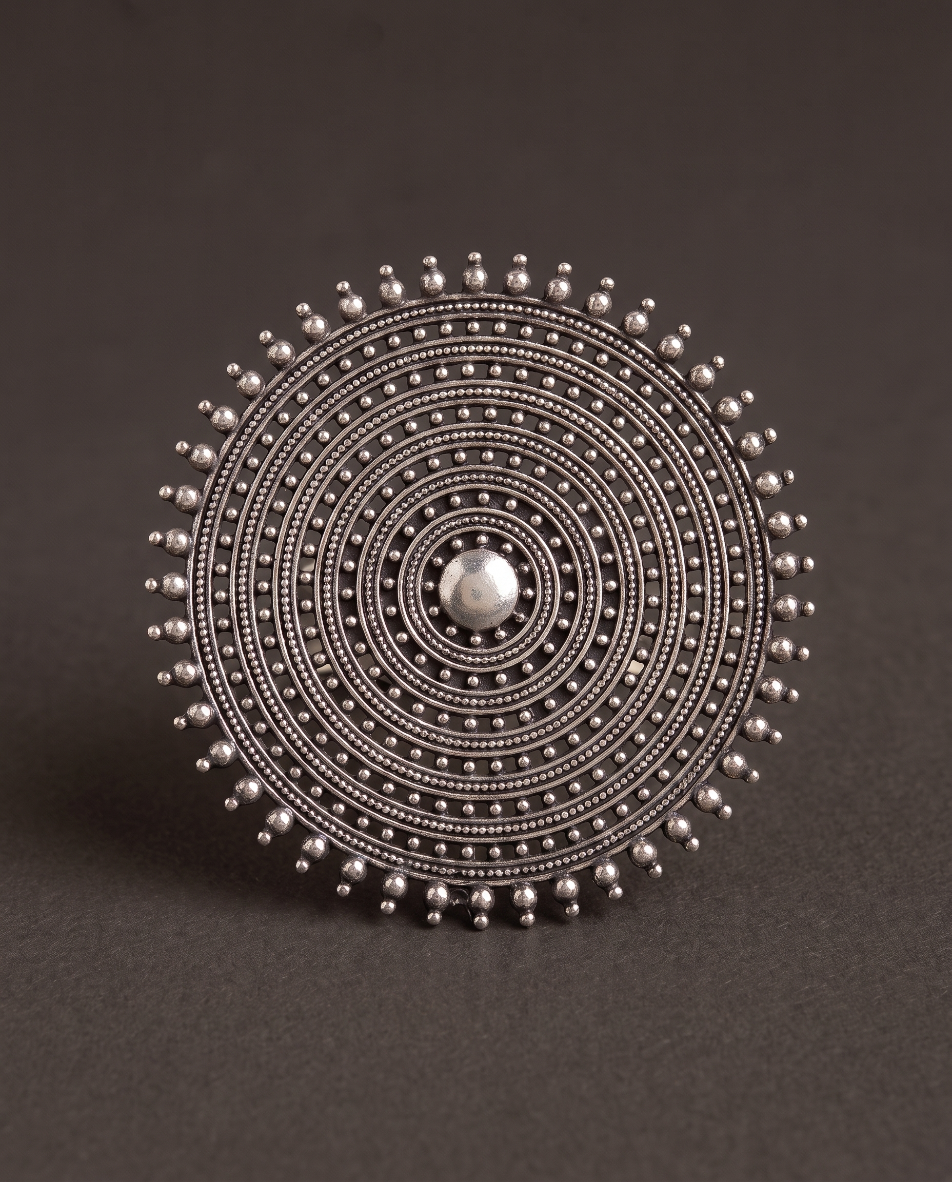 Close-up of the Nishan concentric disc ring on charcoal, showing the fine beaded granulation and smooth domed centre