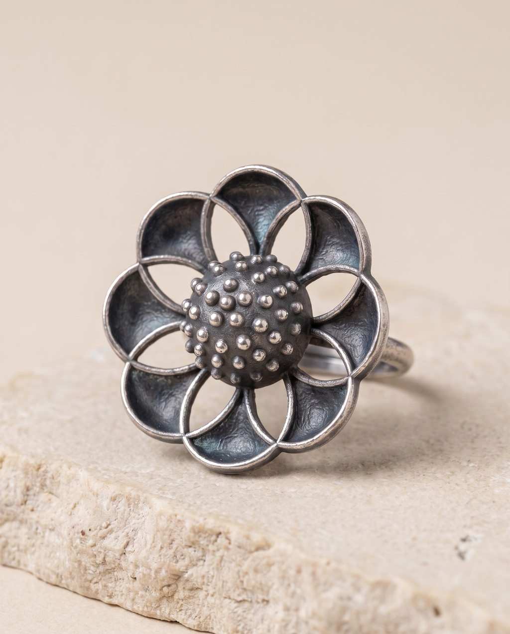 Close-up of the Vibha flower ring on pale limestone, showing the dished petal panels against the rough granulated dome