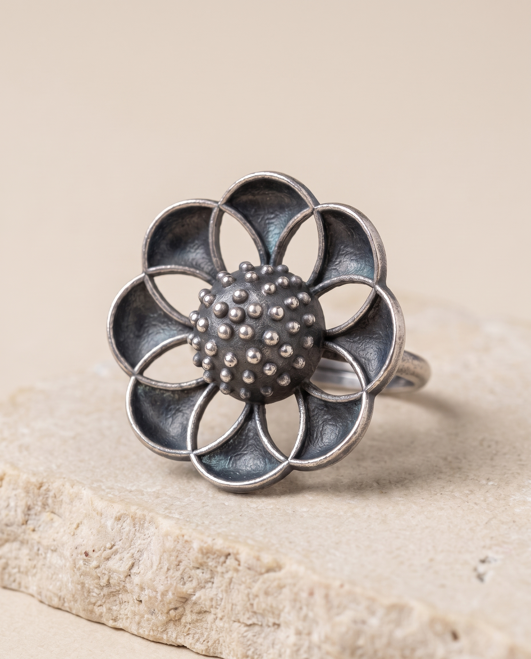 Close-up of the Vibha flower ring on pale limestone, showing the dished petal panels against the rough granulated dome
