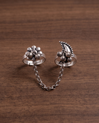 Close-up of the Pushkara two-finger ring on dark walnut wood, showing the rollo chain links and hanging ghungroo bells