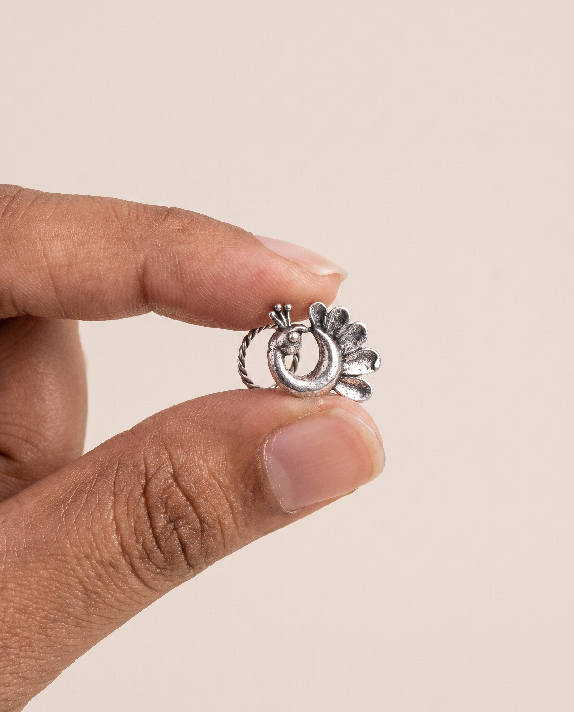 Morni peacock piercing nose pin held between fingertips in profile, showing its small size and its fitting