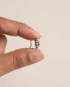 Phool floral disc nose pin held between fingertips in profile, showing its small size and its fitting