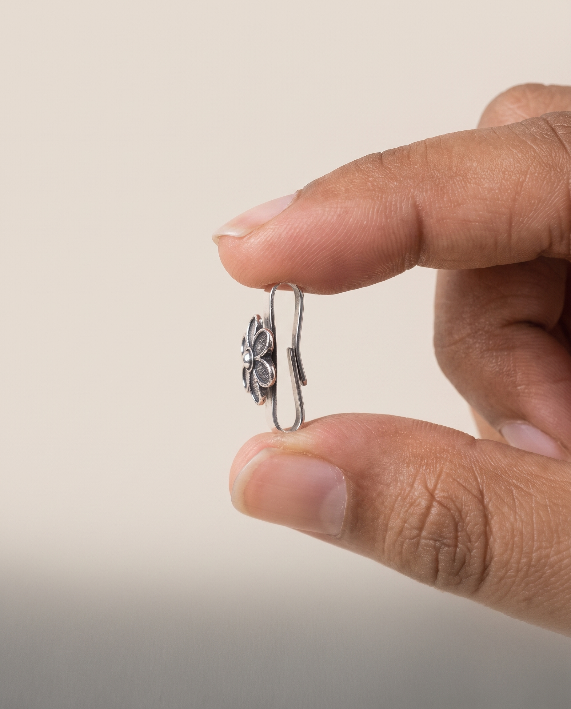 Lily nose pin held between fingertips in profile, showing its small size and the flat U-shaped clip that needs no piercing