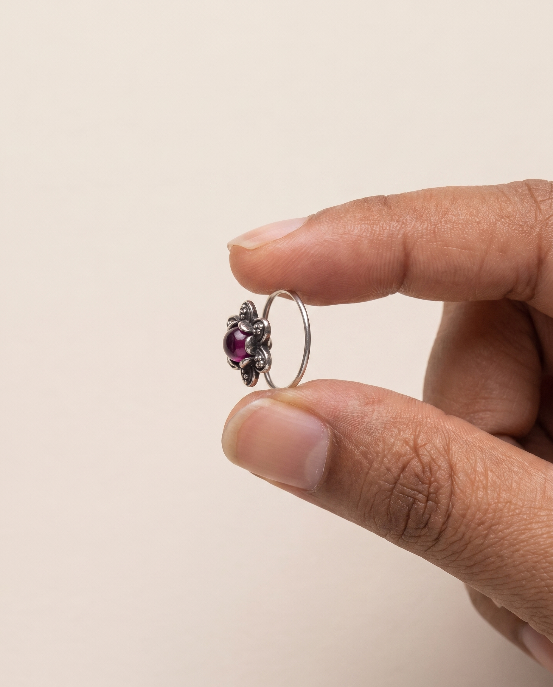 Divi nose pin held between fingertips in profile, showing its small size and the curved wire piercing fitting