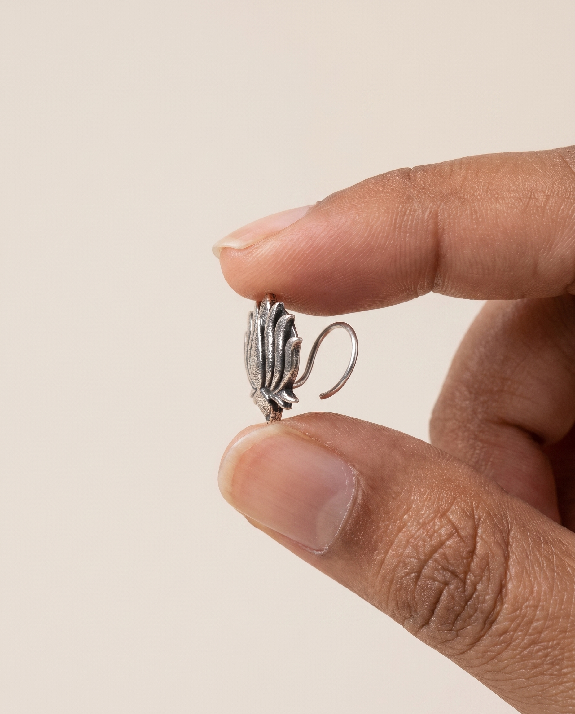 Kamal lotus nose pin held between fingertips in profile, showing its small size and the curved wire piercing fitting