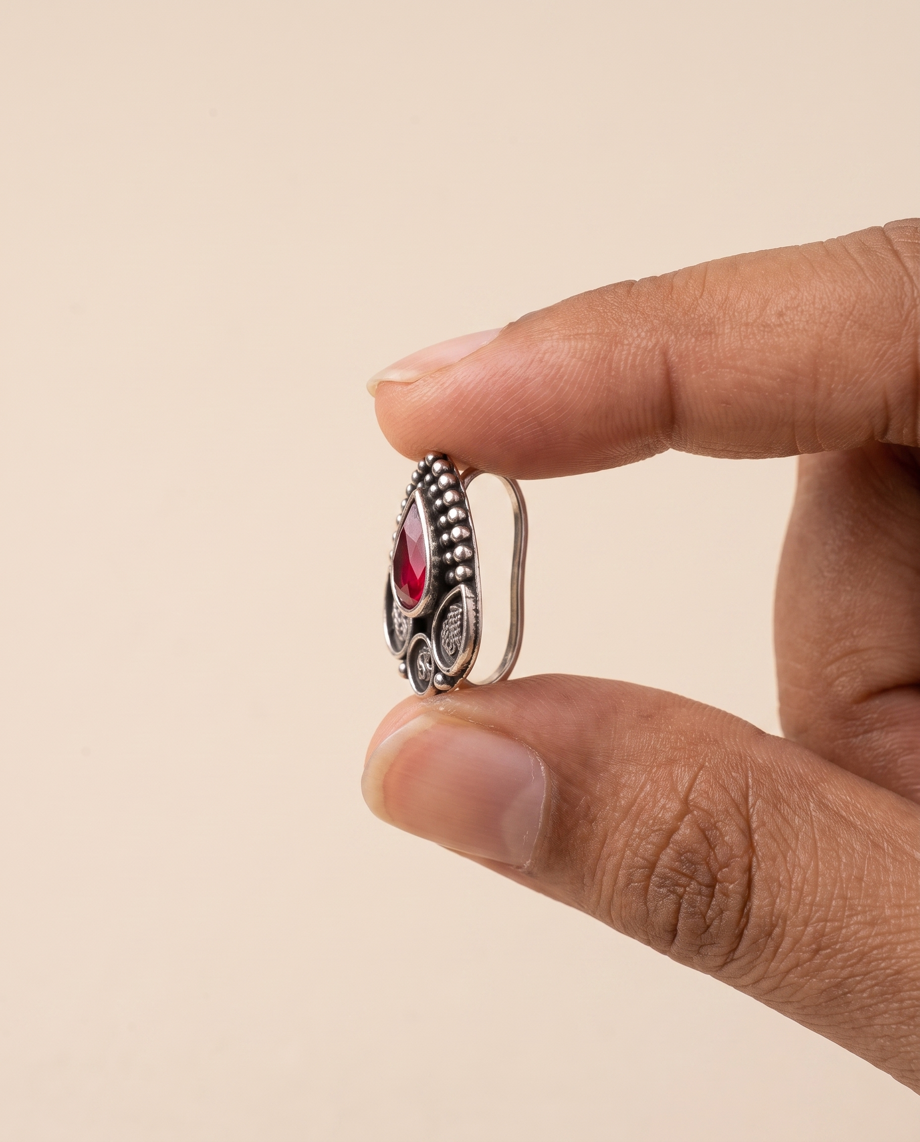 Zari teardrop nose pin held between fingertips in profile, showing its small size and its fitting