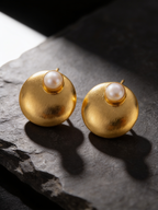 Gold-tone freshwater pearl dome stud earrings on a dark background