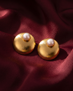 Gold-tone anti-tarnish brass stud earrings each set with a domed freshwater pearl, styled on burgundy silk
