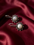 Silver-tone anti-tarnish brass drop earrings each set with a freshwater pearl, styled on burgundy silk