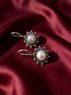Silver-tone anti-tarnish brass drop earrings each set with a freshwater pearl, styled on burgundy silk