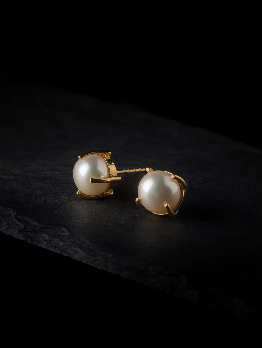 Gold-tone freshwater pearl stud earrings on a dark background