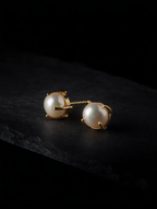 Gold-tone freshwater pearl stud earrings on a dark background