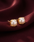 Gold-tone anti-tarnish brass stud earrings each set with a single freshwater pearl, styled on burgundy silk