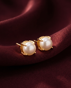 Gold-tone anti-tarnish brass stud earrings each set with a single freshwater pearl, styled on burgundy silk