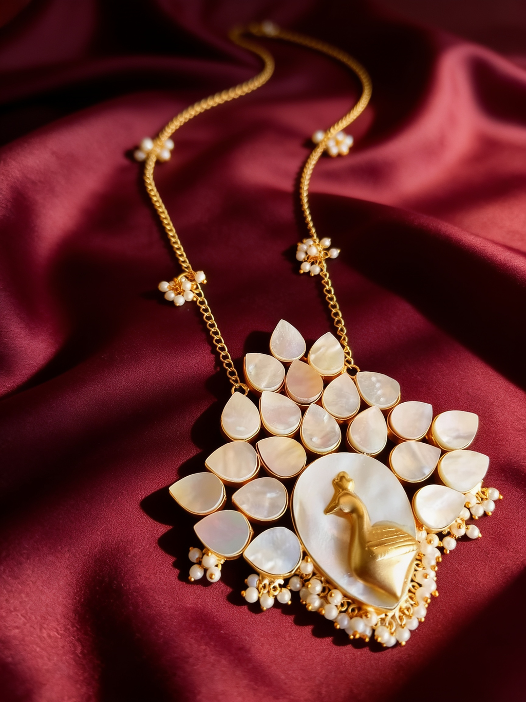 Gold-tone anti-tarnish brass necklace and earrings set with a mother-of-pearl peacock motif and pearls, styled on burgundy silk