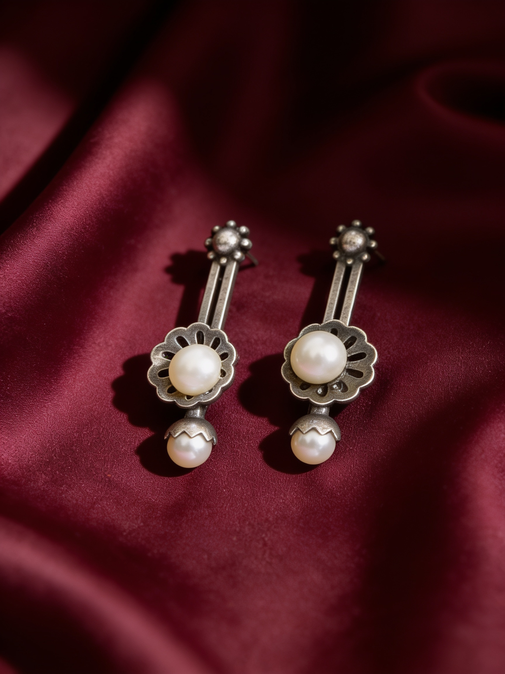 Oxidised silver-look brass earrings with an understated minimal shape, styled on burgundy silk