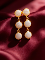Gold-tone anti-tarnish brass earrings each set with three pearls in a vertical row, styled on burgundy silk